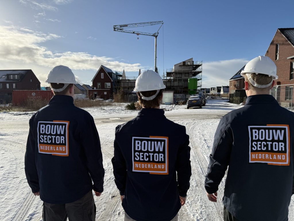 Teamleden in bedrijfskleding van Bouwsector Nederland kijken uit over besneeuwde nieuwbouwhuizen