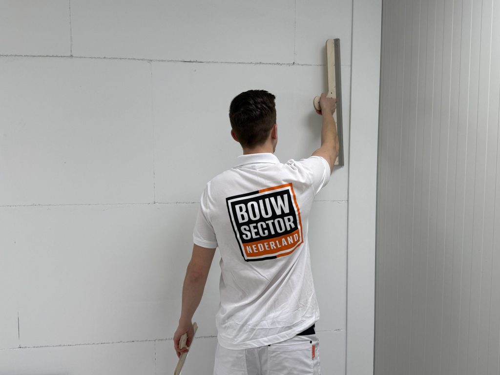 Stukadoor in wit werkpak trekt met een lange spaan een wand strak